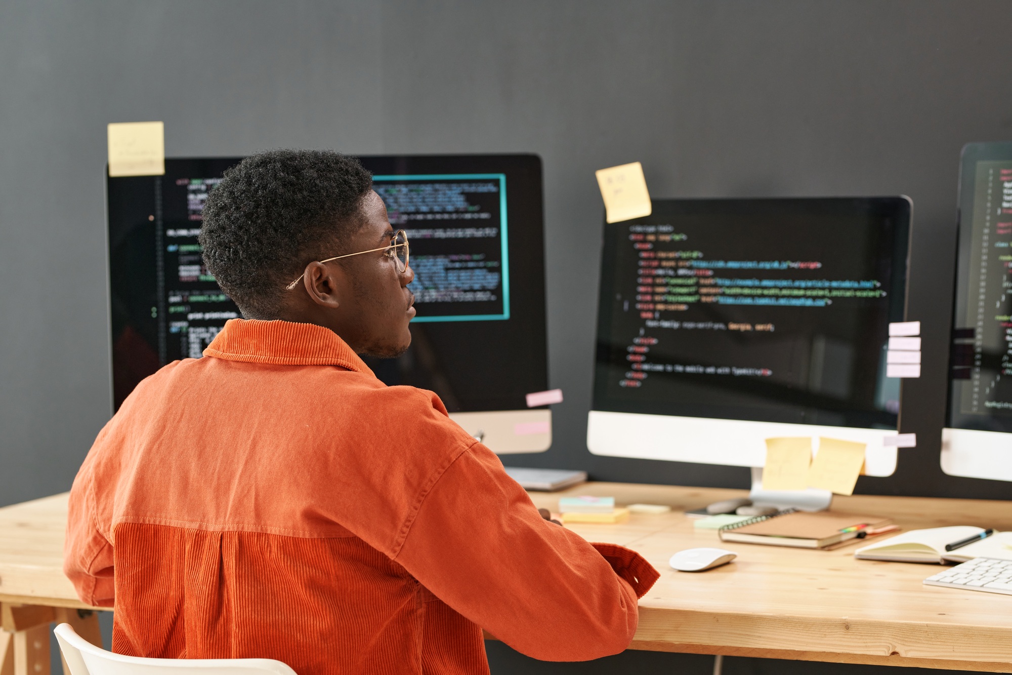 Rear view of young black man concentrating on decoding data on computer screen