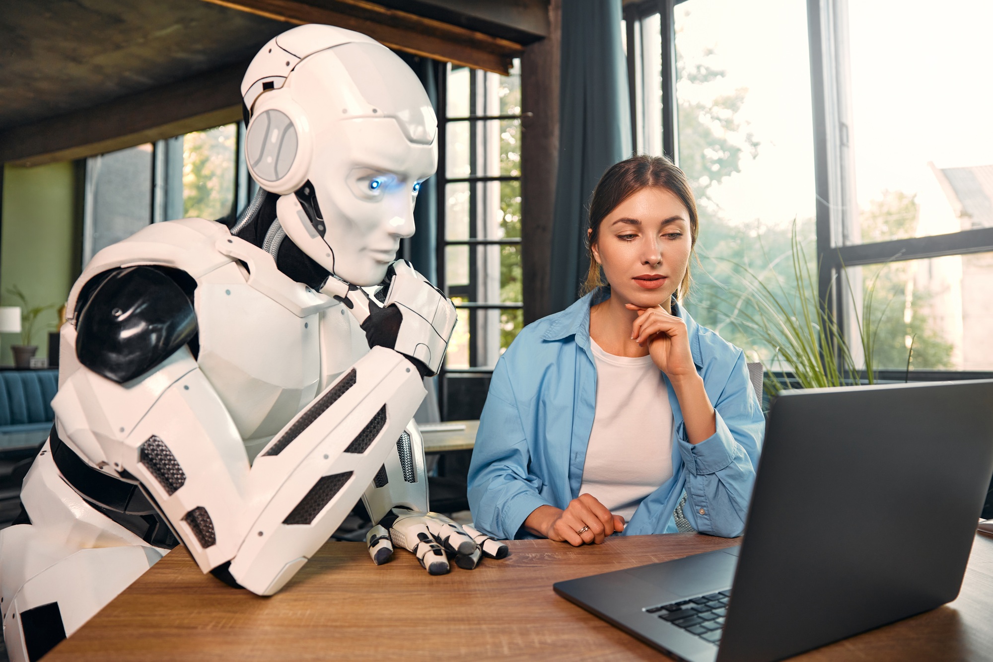 Robot and woman working on laptop in office